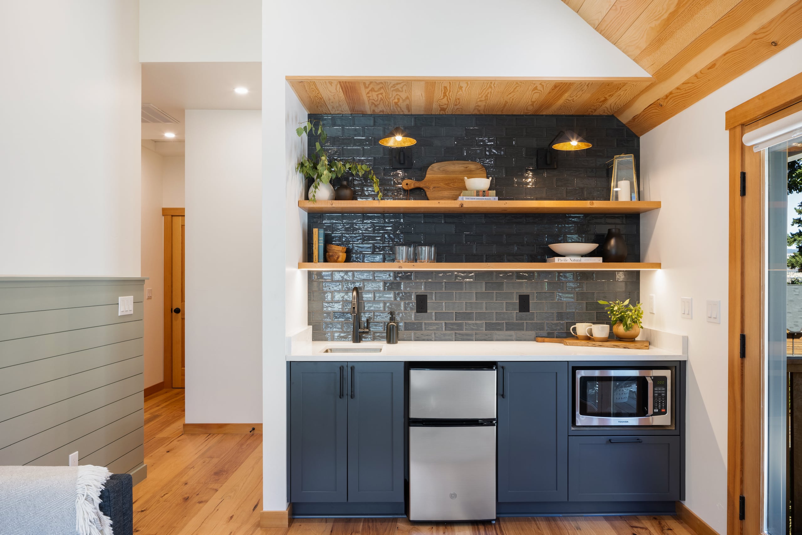 a kitchenette with elegant blue tile, navy cabinets, and exposed wood